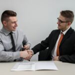 deux hommes se faisant face tout en se serrant la main et en souriant